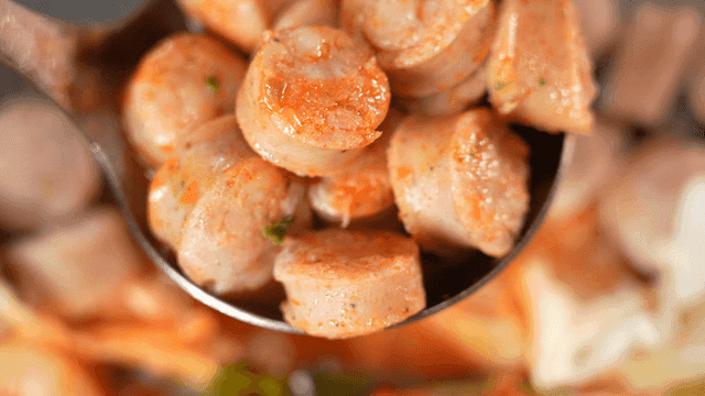 Ladle filled with sauce-coated stir-fried sausage