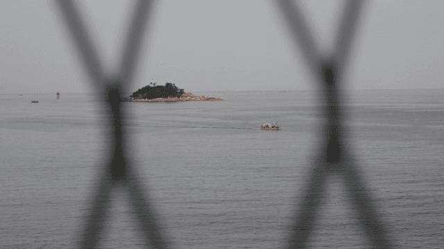 철망 넘어 보이는 등대가 있는 작은 섬과 배