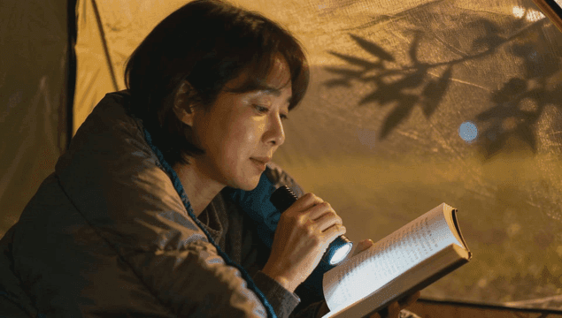 텐트 안에서 손전등으로 책을 읽는 중년 여성