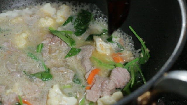 Pouring soy sauce into a pan and stir-frying vegetables and meat