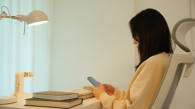 Woman using a smartphone at a desk in a calmly lit room