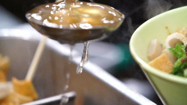 Pouring the broth into a bowl with the fish cakes and spicy sauce