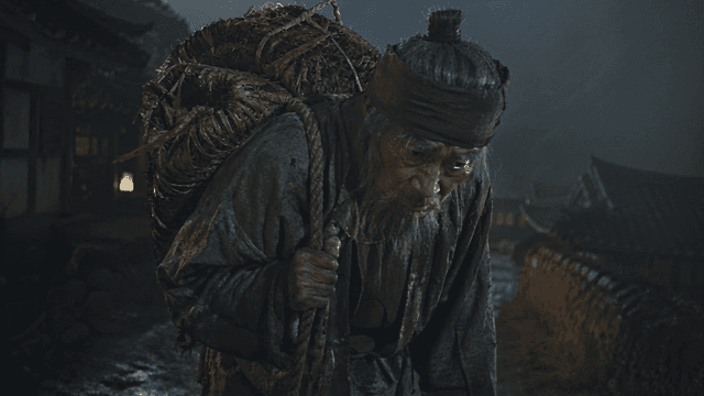 An elderly man carrying a heavy load at night