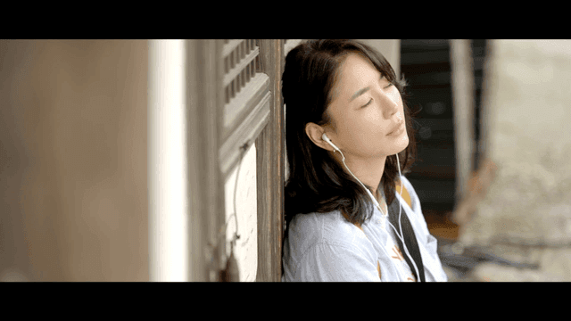 Woman listening to music while leaning against Hanok door