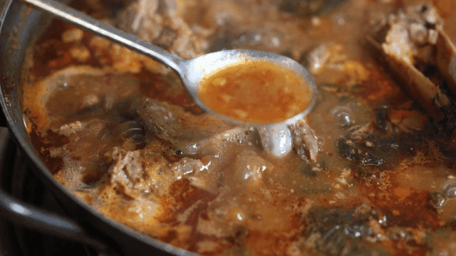 Spoon scooping out boiling gamjatang broth from pot