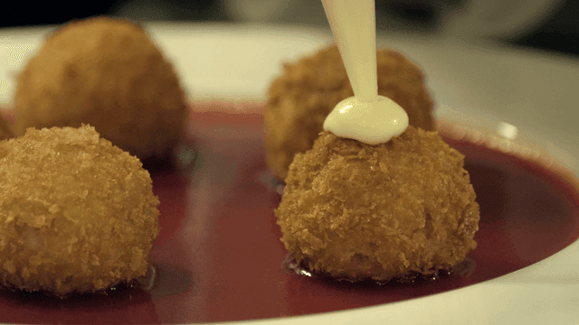 Sauce being poured on fried croquettes