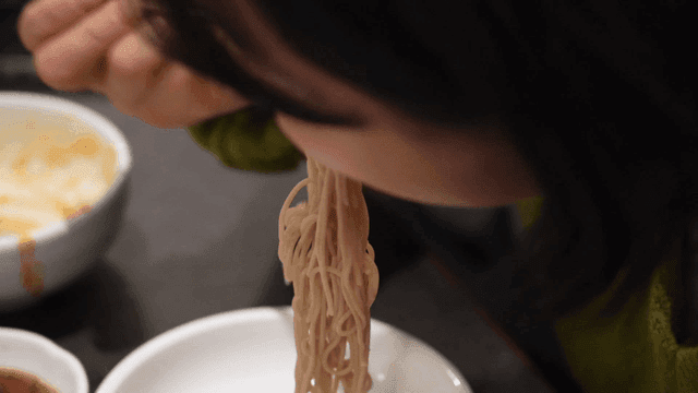 Woman eating mouthful of cold noodles with meat