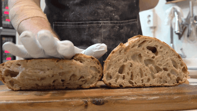 Baker pressing freshly baked campagne bread on wooden board