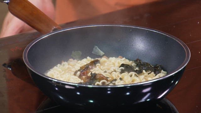 프라이팬에서 끓는 라면 사리 위에 감칠맛을 더해줄 스프를 뿌리는 모습