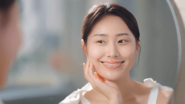 Woman smiling and touching face in front of mirror indoors