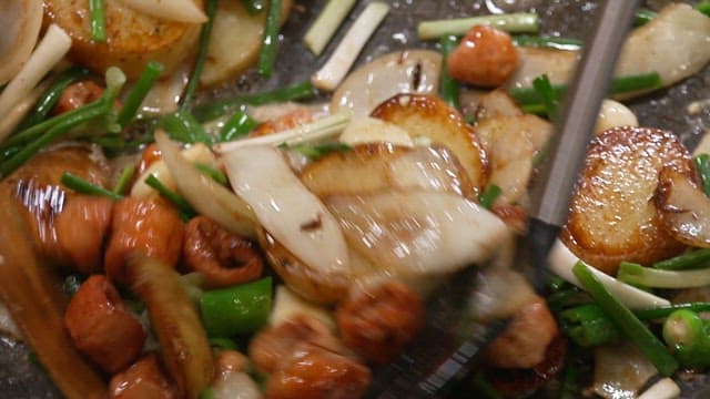 Grilled pork intestines being cooked in a frying pan with garlic and green onions