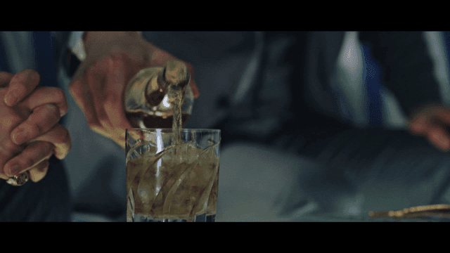 Man in suit pouring whiskey into glass with ice