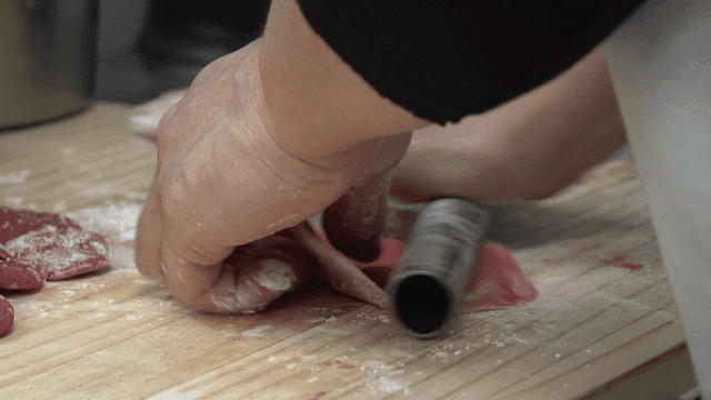 Hands pushing dumpling wrappers on wooden cutting board