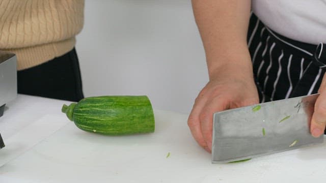 Chef chopping green zucchini on a white cutting board