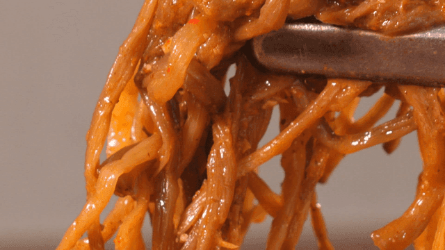 Sweet potato stems from pork backbone stew being lifted with tongs