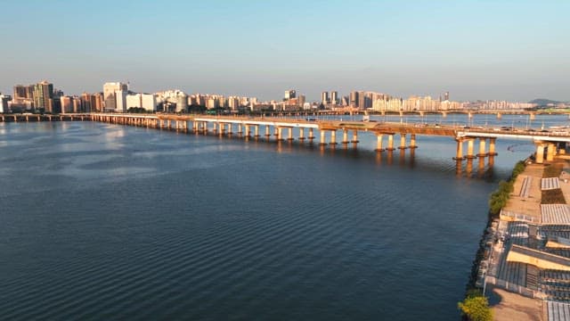 Long bridge over a tranquil river with city skyline