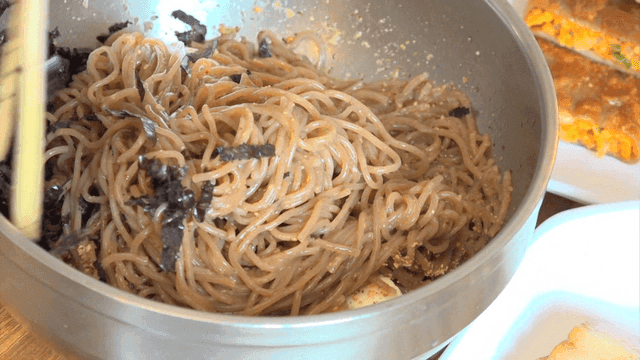 Chopsticks mixing perilla oil makguksu with egg and seaweed