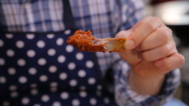 Person wearing an apron eating spicy braised ribs