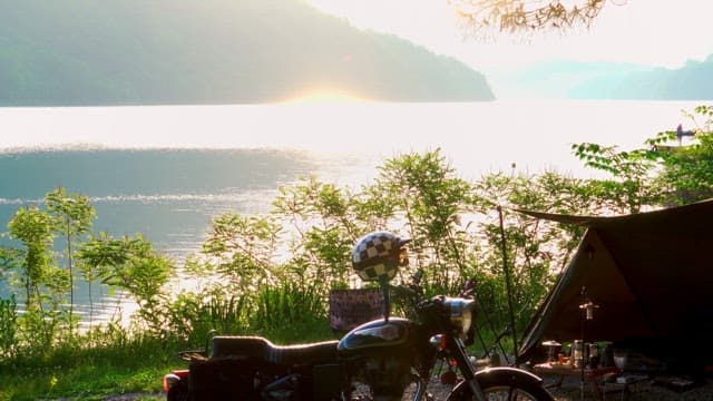 Campsite by a serene lake at sunrise with motorbike and tent