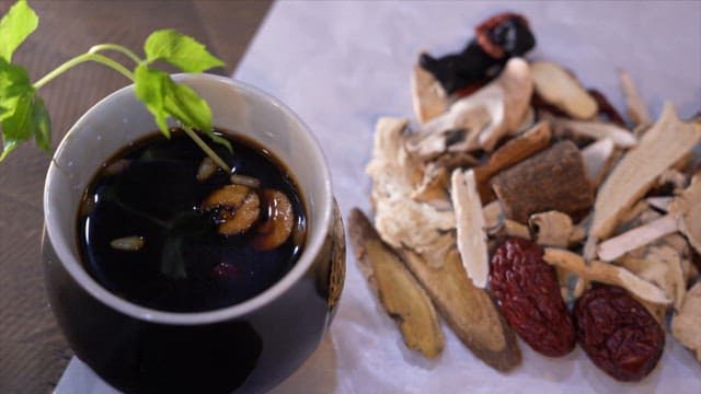 나무 테이블 위의 한약이 든 컵과 한약재가 있는 모습