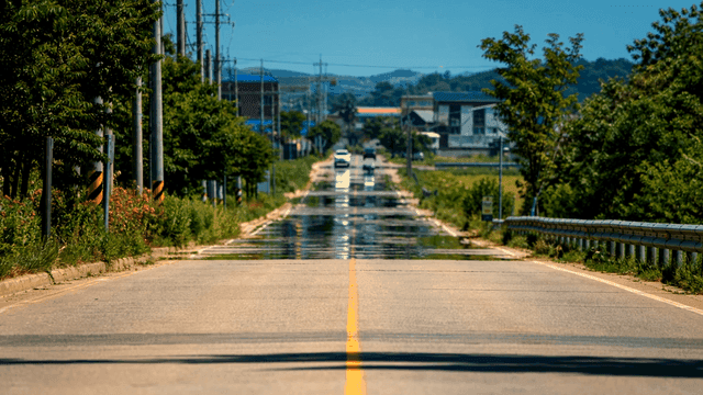 Country road with heat haze where cars are visible in distance