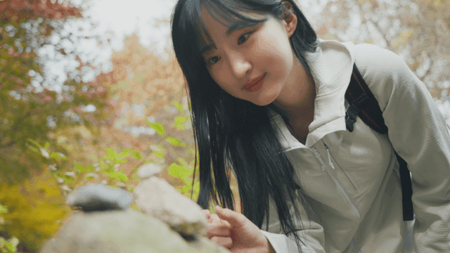 Woman in hiking clothes stacking stones in autumn forest