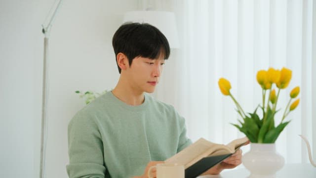 Man reading a book and drinking coffee in a bright room