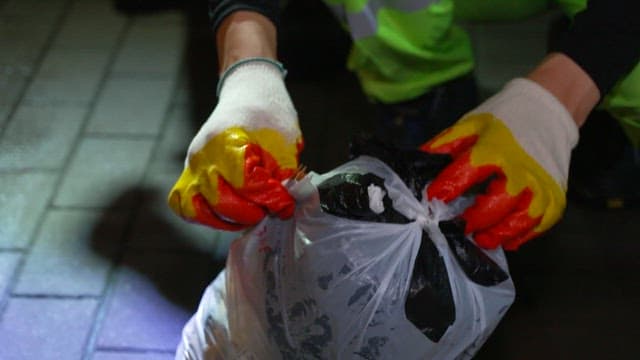 Person tying a garbage bag in an industrial area at night