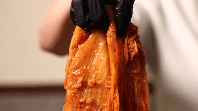 Kimchi stew lifted with gloved hands