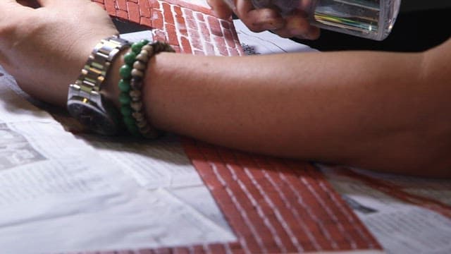 Spraying glue with a sprayer onto cardboard with a brick pattern