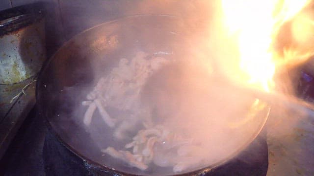 Stir-frying ingredients in a wok with flames