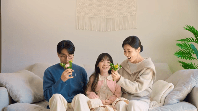 소파에 앉아있는 부모님께 카네이션을 선물하는 아이