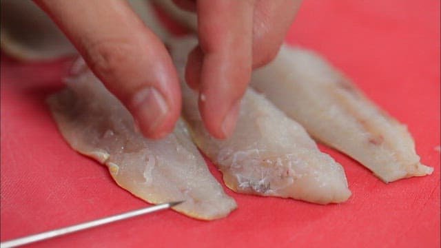 Hand preparing fish fillets on skewers