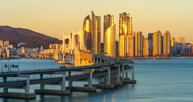 From evening to night view of a bustling port city Busan with tall skyscrapers and Gwangan Bridge