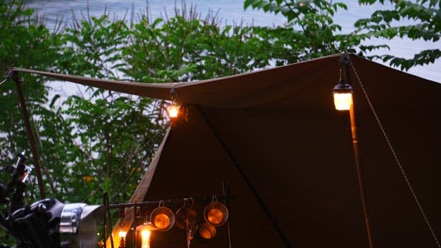 Lantern-lit tent in campsite in the evening by the lake