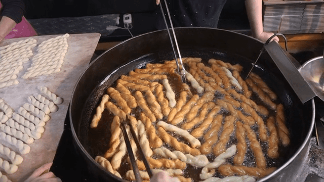 Twisted doughnuts frying in a large pan