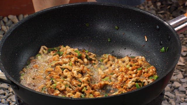 Sprinkling red pepper powder on top of sea eel stir-fried in a frying pan