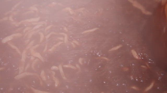 Stirring red bean noodles boiling in a pot with wooden spatula