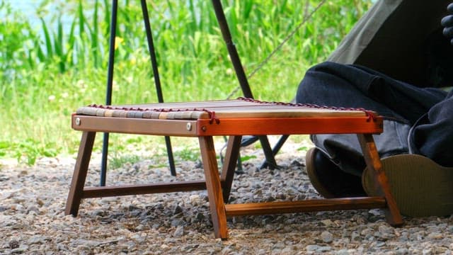 Man setting up a small wooden stool outdoors near a tent on a gravels