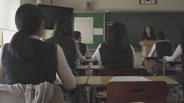 Students in school uniforms in a classroom attentively listening to a teacher