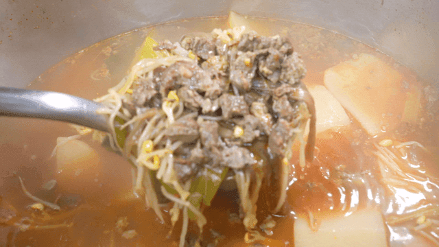 Ladle scooping beef soup from boiling pot