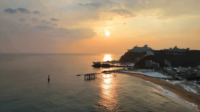 Sunset on tranquil beach with boat-shaped hotel visible in distance