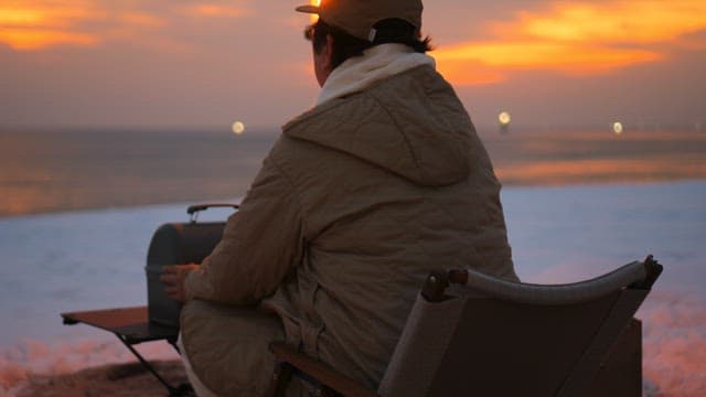 Man sitting on the beach at sunset preparing cook in winter