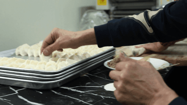 Hands of people making dumplings in kitchen and placing them on tray