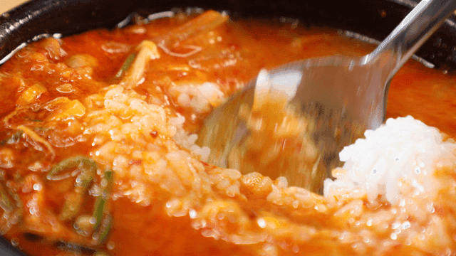 Spoon mixing rice into earthenware pot soybean paste stew