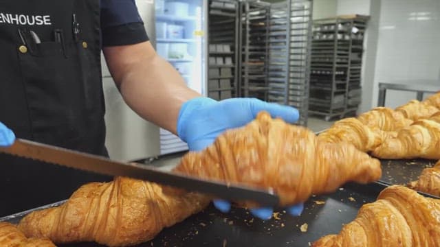 Baker slicing freshly baked croissants in a commercial kitchen