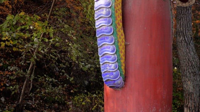 숲속 빨간 기둥에 있는 나무로 만든 생생한 색상의 용 조각상