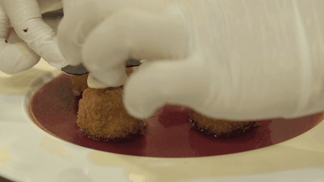 Chef garnishing croquettes with sauce