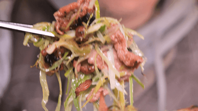 Chopsticks picking up steaming charcoal-grilled green onion bulgogi