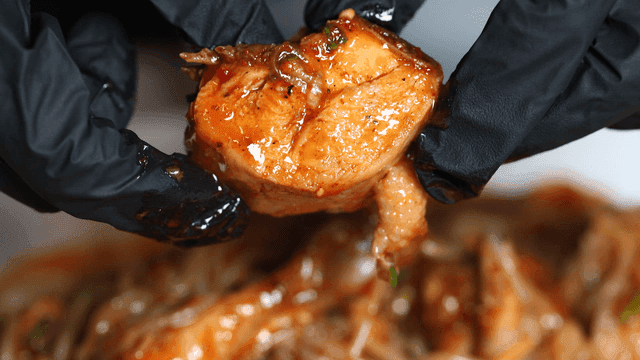 Spicy braised chicken lifted with gloved hands